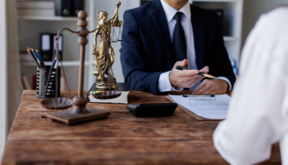Attorney at a desk with a Lady Justice statue discussing a contract with a client