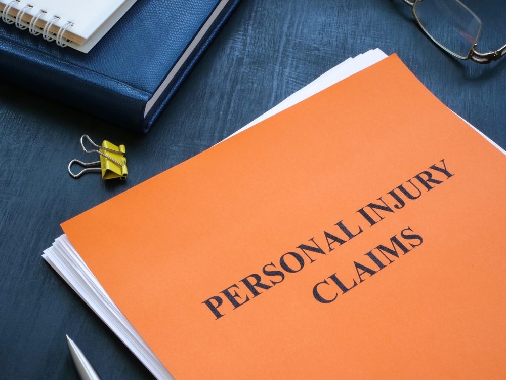 Orange "Personal Injury Claims" file folder on a desk with a notebook, glasses, and pen