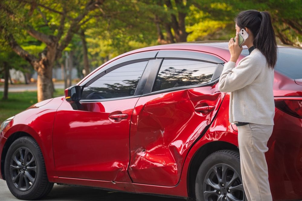 Woman on the phone next to her damaged red car after a crash