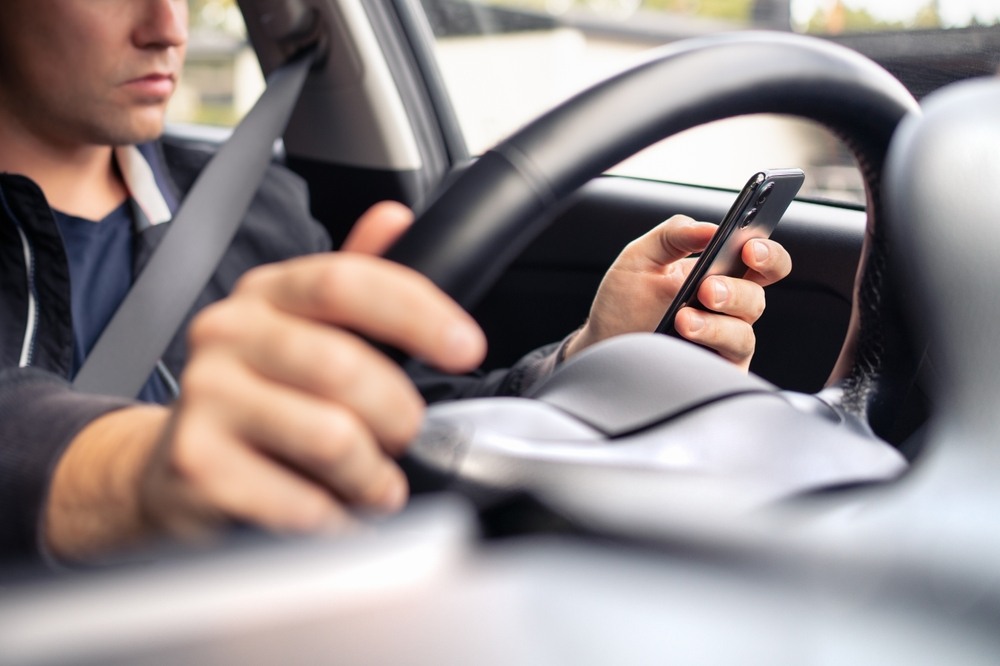 Driver holding smartphone and steering wheel while distracted behind the wheel