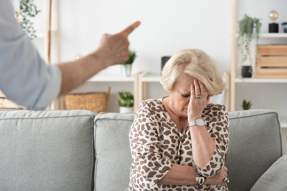 Elderly woman looking distressed while someone points and yells at her
