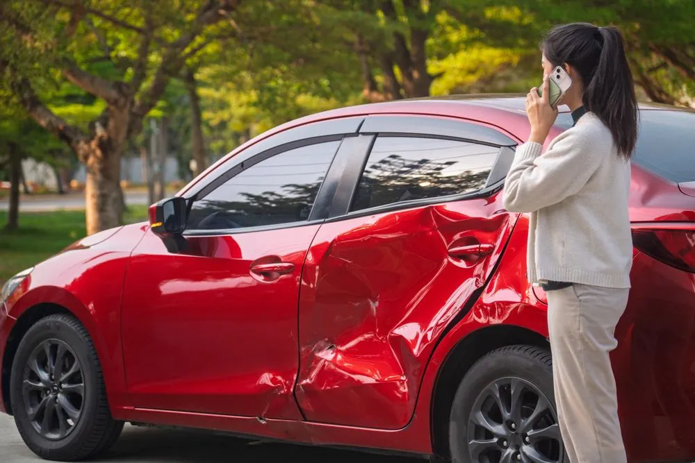 Woman on the phone next to her damaged red car after a crash